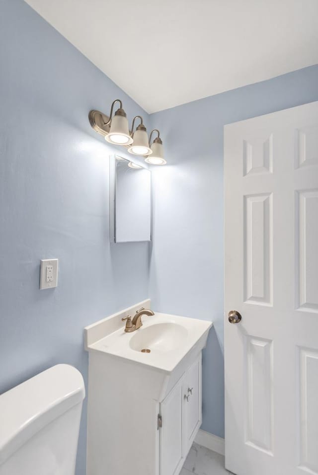 half bath with toilet, marble finish floor, and vanity