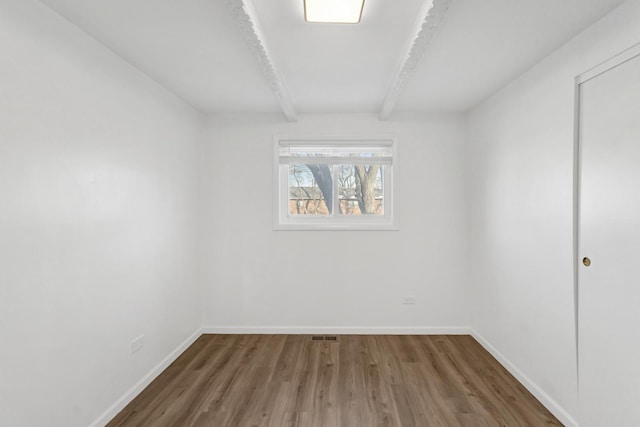 empty room featuring beamed ceiling, wood finished floors, and baseboards