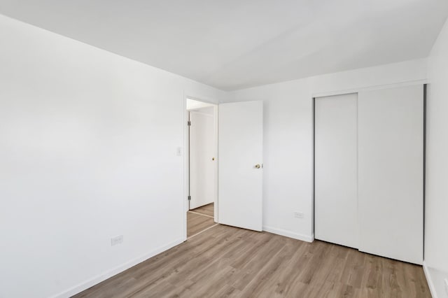 unfurnished bedroom featuring light wood-style flooring, baseboards, and a closet