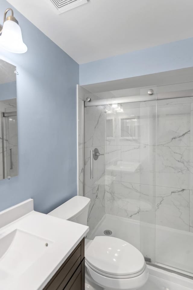 bathroom featuring visible vents, vanity, a marble finish shower, and toilet