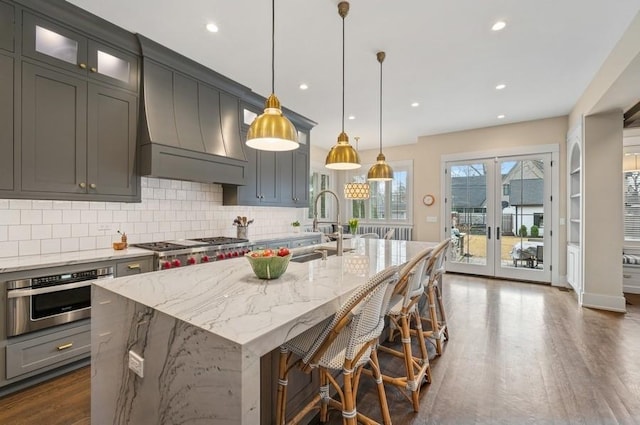 kitchen featuring dark wood finished floors, a center island with sink, stainless steel oven, a sink, and premium range hood