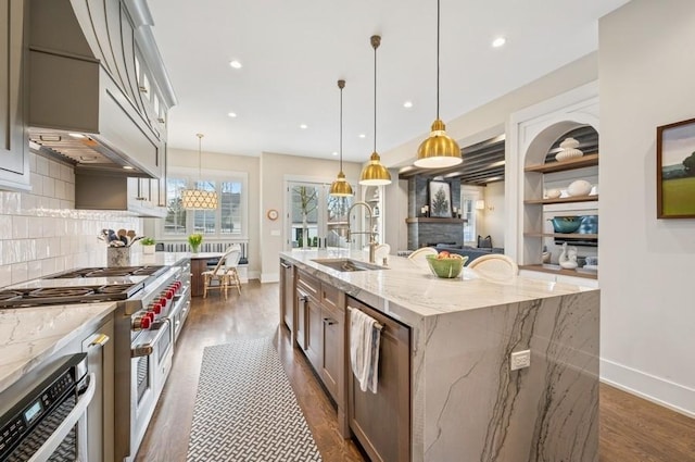 kitchen featuring a kitchen island with sink, a sink, appliances with stainless steel finishes, backsplash, and pendant lighting