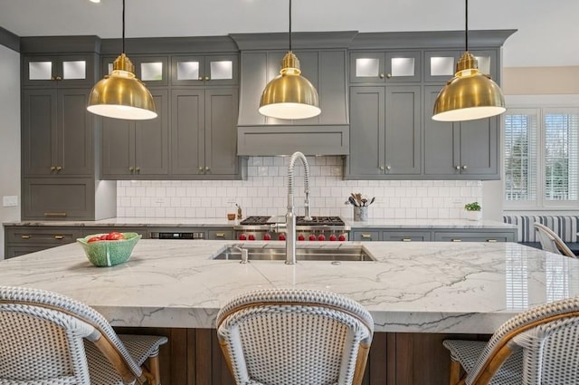 kitchen with a breakfast bar area, light stone countertops, tasteful backsplash, an island with sink, and pendant lighting