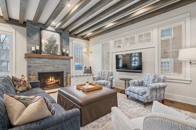 living room featuring visible vents, baseboards, wood finished floors, a fireplace, and beam ceiling