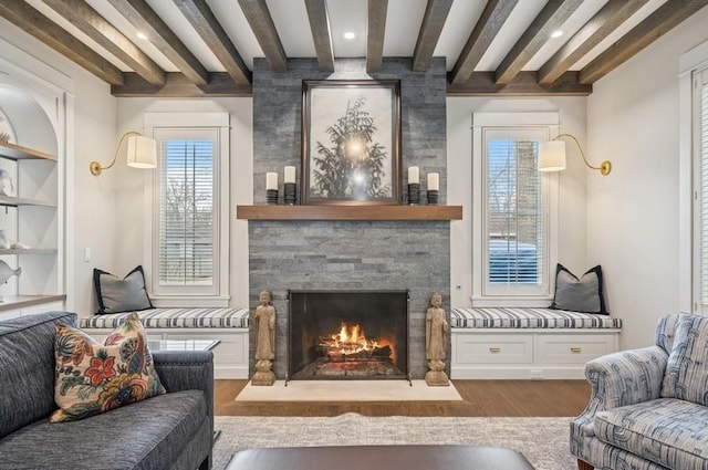 living area featuring beam ceiling, a stone fireplace, and wood finished floors