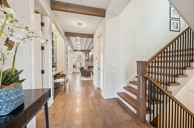 entrance foyer with beam ceiling, wood finished floors, a warm lit fireplace, baseboards, and stairs