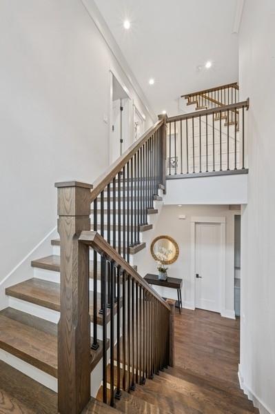 staircase featuring a towering ceiling, baseboards, wood finished floors, and recessed lighting