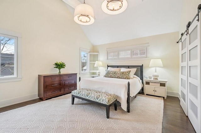 bedroom with high vaulted ceiling, wood finished floors, multiple windows, and a barn door