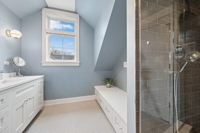 bathroom featuring lofted ceiling, a tile shower, vanity, and baseboards