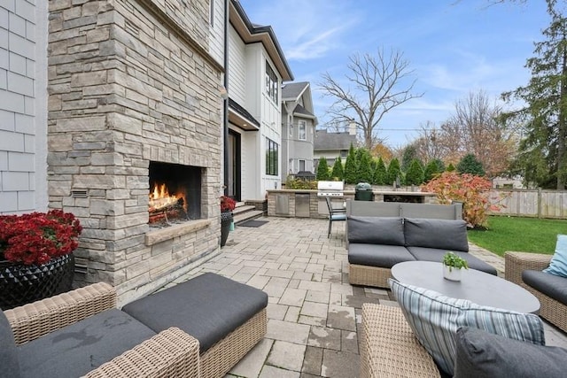 view of patio featuring fence, an outdoor kitchen, an outdoor living space with a fireplace, and grilling area