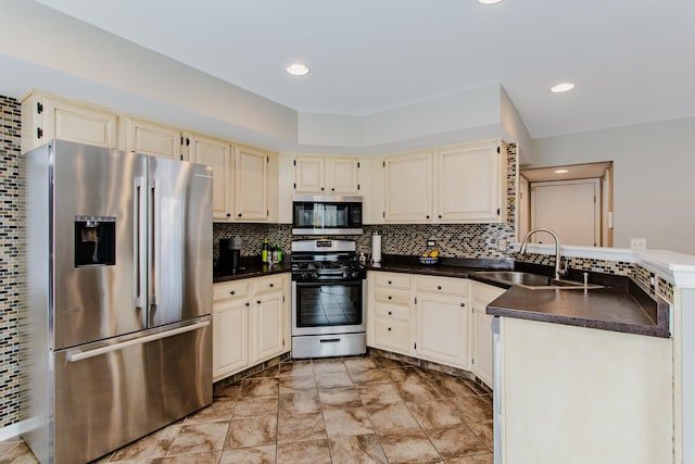 kitchen featuring stainless steel appliances, dark countertops, cream cabinets, decorative backsplash, and a sink