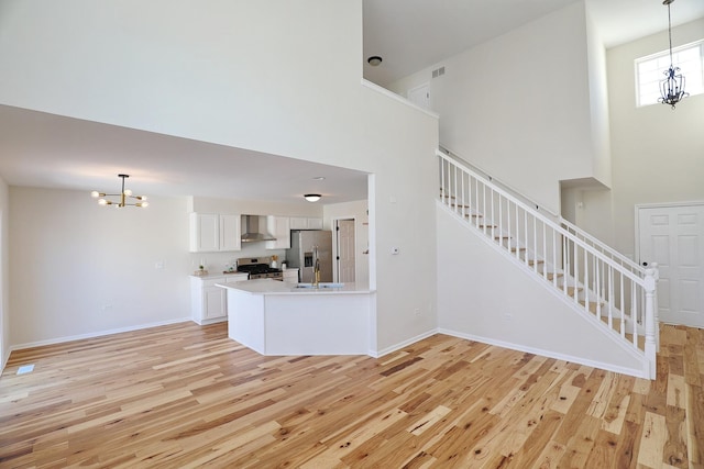 unfurnished living room with stairs, light wood-type flooring, a chandelier, and a towering ceiling