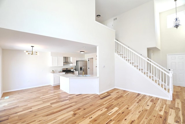 unfurnished living room featuring a towering ceiling, light wood finished floors, a notable chandelier, and stairway