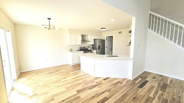 kitchen with stainless steel appliances, light wood finished floors, a sink, and wall chimney range hood