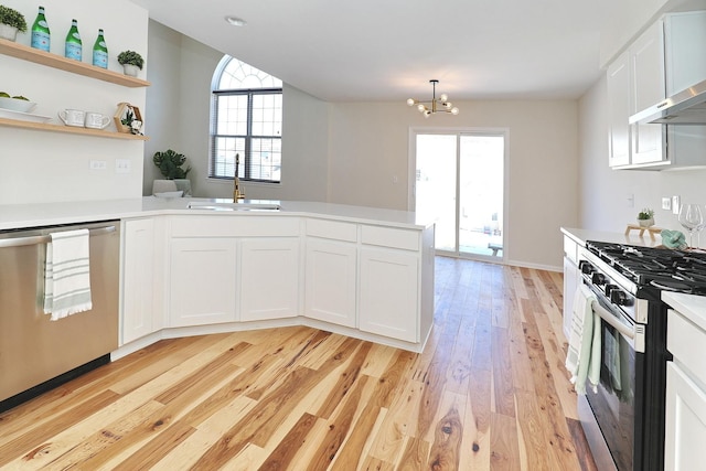 kitchen with wall chimney range hood, light countertops, a sink, stainless steel appliances, and light wood finished floors