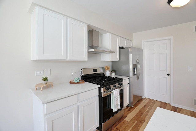 kitchen with light wood finished floors, wall chimney exhaust hood, stainless steel appliances, light countertops, and white cabinetry