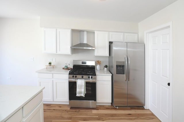 kitchen featuring stainless steel appliances, light wood-style floors, white cabinetry, and wall chimney range hood
