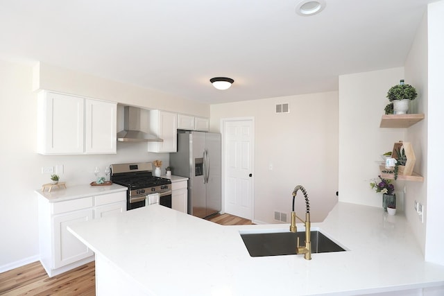 kitchen with wall chimney range hood, a peninsula, visible vents, stainless steel appliances, and a sink