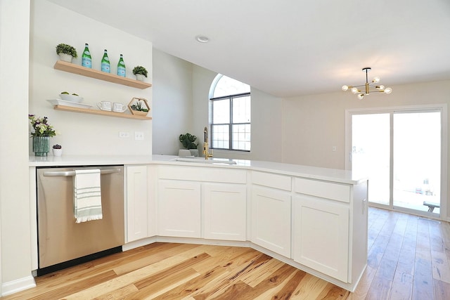kitchen featuring an inviting chandelier, a sink, light countertops, a peninsula, and stainless steel dishwasher