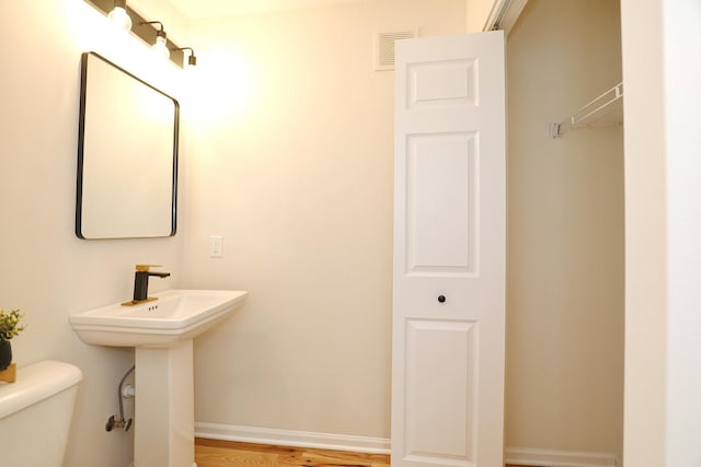 half bath featuring toilet, wood finished floors, visible vents, a sink, and baseboards