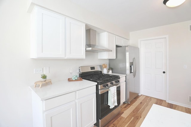 kitchen with wall chimney range hood, light countertops, light wood-type flooring, appliances with stainless steel finishes, and white cabinetry