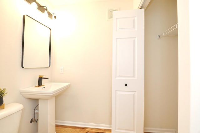 half bath with visible vents, toilet, wood finished floors, a sink, and baseboards