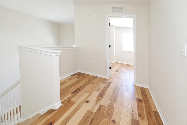 hall with an upstairs landing, visible vents, light wood-type flooring, and baseboards