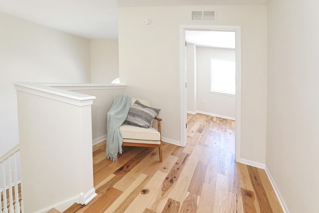 unfurnished room featuring light wood-type flooring, an upstairs landing, and visible vents
