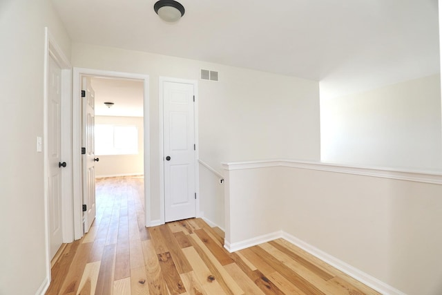 corridor with an upstairs landing, light wood-style flooring, baseboards, and visible vents