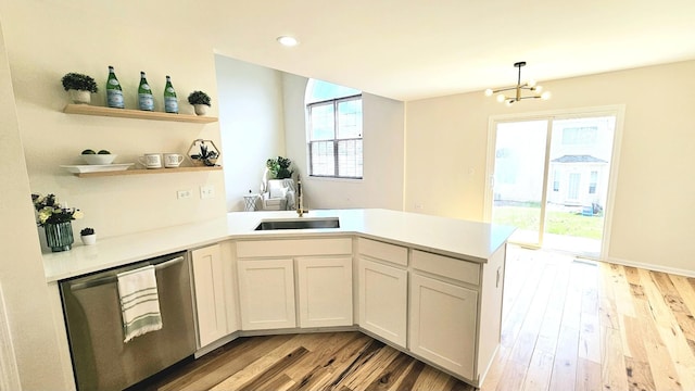 kitchen with open shelves, a sink, a peninsula, light wood finished floors, and stainless steel dishwasher