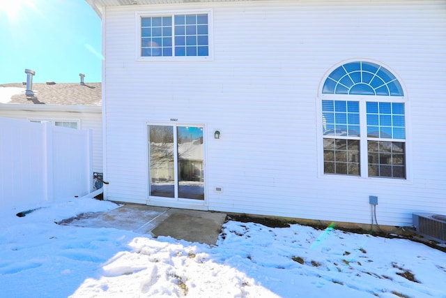 snow covered rear of property featuring cooling unit and fence