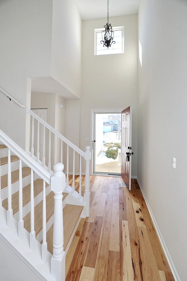 foyer entrance with light wood-style flooring, baseboards, a towering ceiling, and stairs