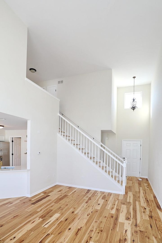 interior space with a notable chandelier, visible vents, a high ceiling, wood finished floors, and baseboards