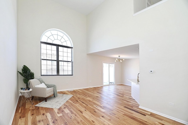 unfurnished room with light wood-style flooring, a high ceiling, a notable chandelier, and baseboards