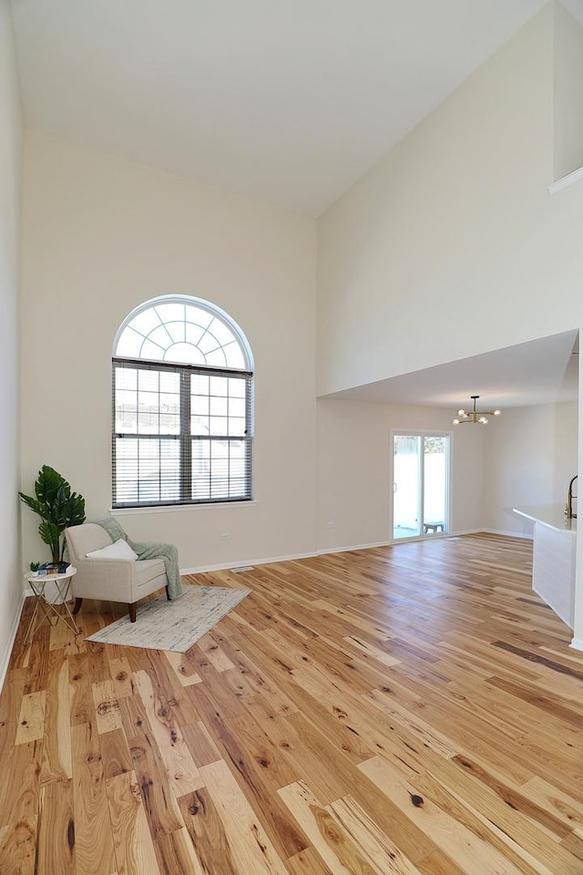 unfurnished room with light wood-style floors, a towering ceiling, and an inviting chandelier