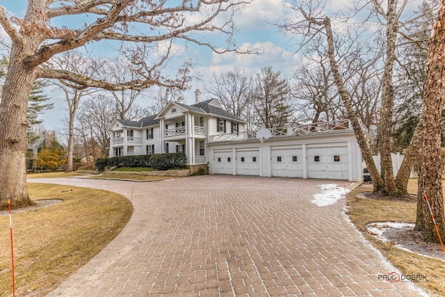 greek revival house with a balcony, a garage, a chimney, and decorative driveway