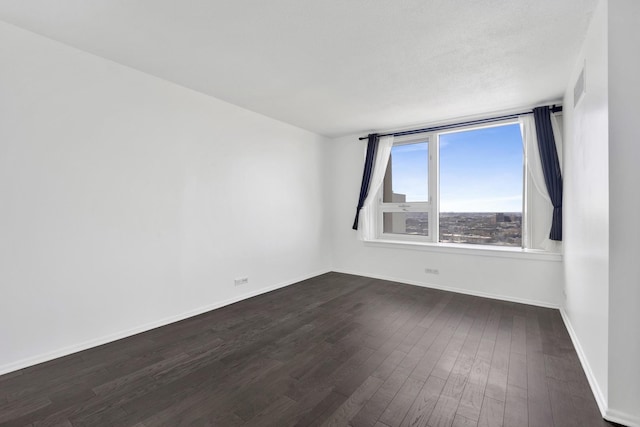 empty room with dark wood-type flooring, visible vents, and baseboards