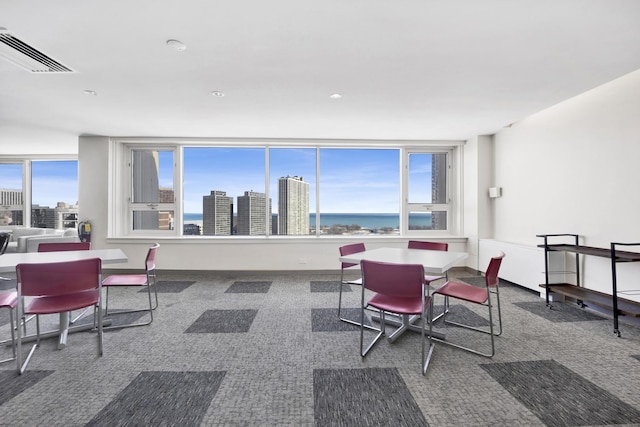 carpeted dining space with a water view, a view of city, and visible vents