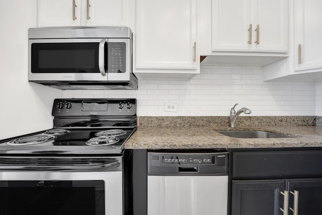 kitchen featuring stainless steel appliances, a sink, white cabinets, light stone countertops, and tasteful backsplash