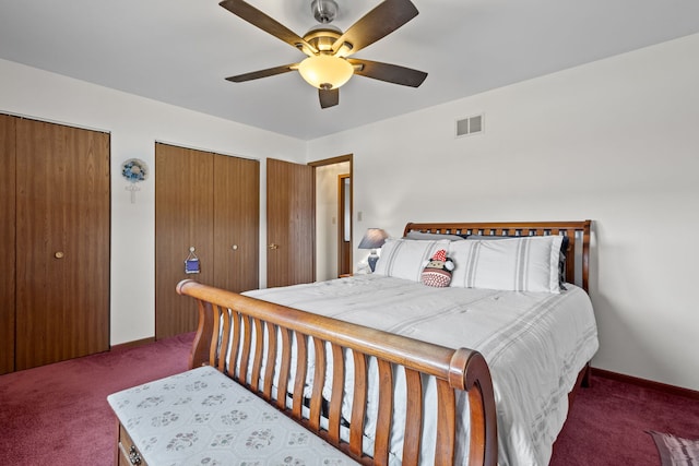 bedroom featuring ceiling fan, visible vents, baseboards, dark carpet, and two closets