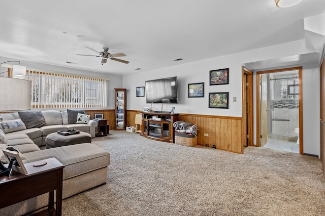 carpeted living area with a wainscoted wall, ceiling fan, visible vents, and wood walls