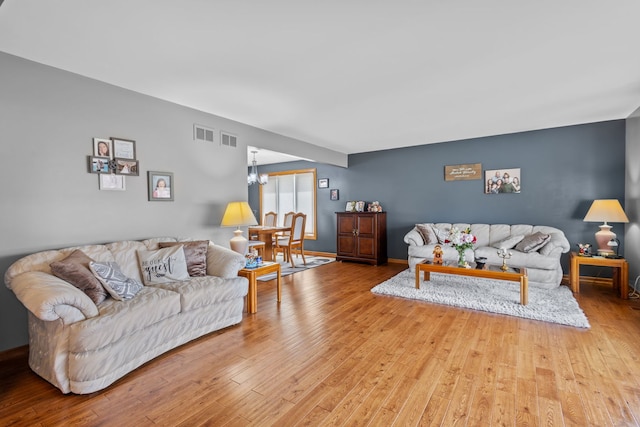 living room featuring baseboards, visible vents, light wood finished floors, and an inviting chandelier