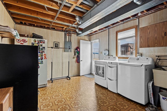 washroom featuring light floors, wood walls, electric panel, and washer and dryer