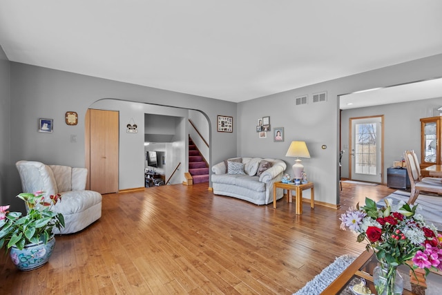 living room with wood-type flooring, stairs, visible vents, and arched walkways