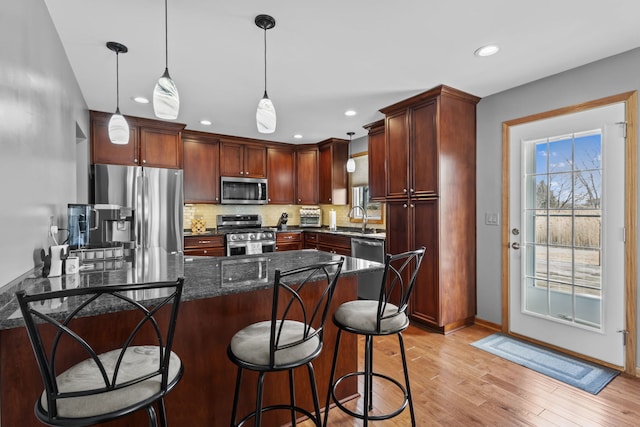 kitchen with pendant lighting, light wood finished floors, stainless steel appliances, tasteful backsplash, and dark stone countertops