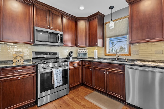 kitchen featuring appliances with stainless steel finishes, dark stone countertops, hanging light fixtures, light wood-style floors, and a sink