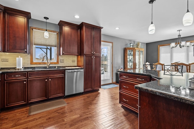 kitchen with dark wood-type flooring, a sink, hanging light fixtures, and stainless steel dishwasher