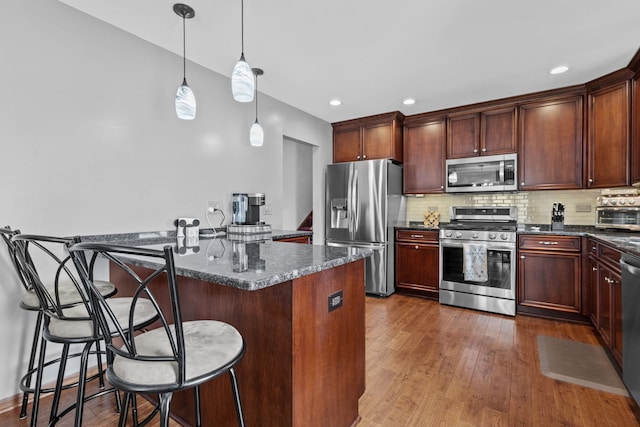 kitchen featuring a kitchen island, appliances with stainless steel finishes, dark stone countertops, a kitchen bar, and decorative light fixtures