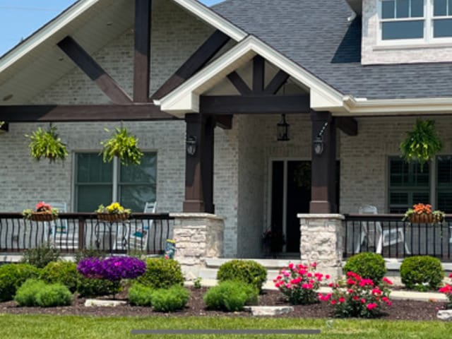 view of exterior entry with covered porch, a shingled roof, and brick siding