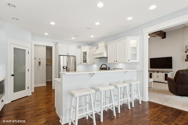 kitchen featuring custom exhaust hood, light countertops, glass insert cabinets, white cabinets, and stainless steel fridge